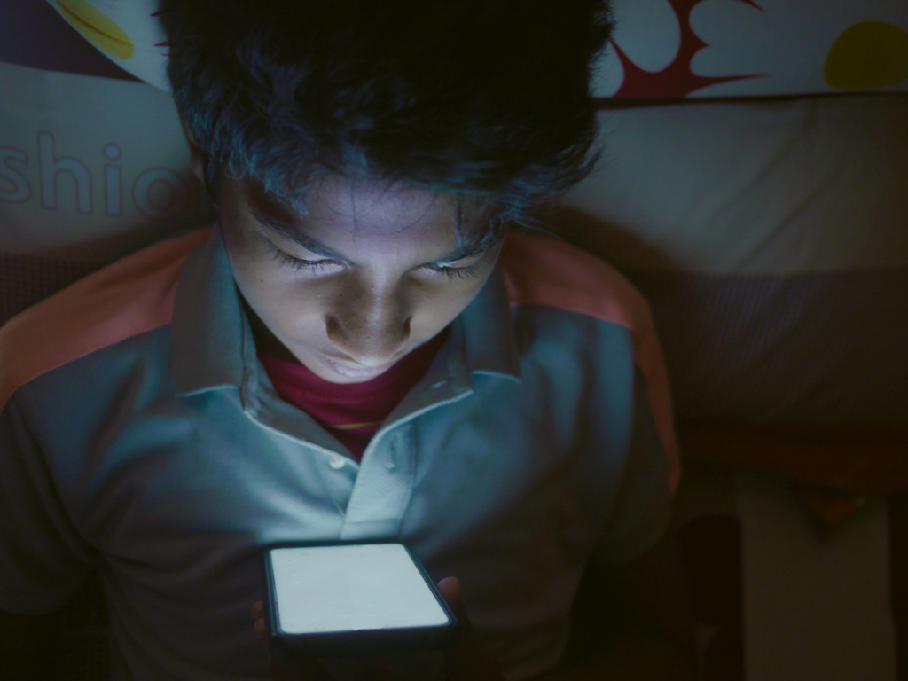 Teenager looking at smartphone screen in the dark, symbolizing online privacy and the need for VPN protection for kids.